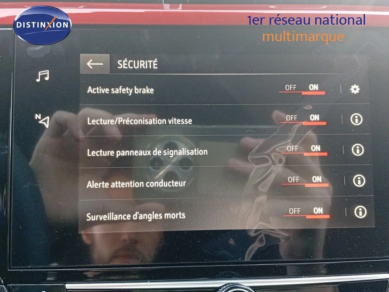 Vue de face rapprochée de l'écran tactile affichant les options de sécurité de l'Opel Corsa rouge Kardio métal avec toit noir.