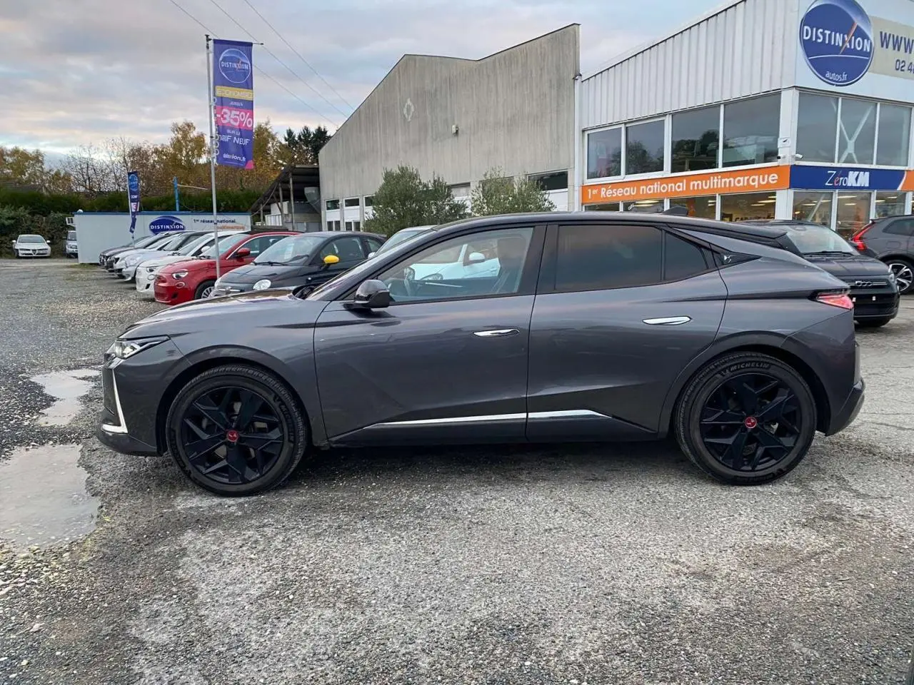 Vue latérale côté gauche d'une DS4 gris platinium 2022 avec jantes noires et lignes épurées, stationnée devant un concessionnaire.