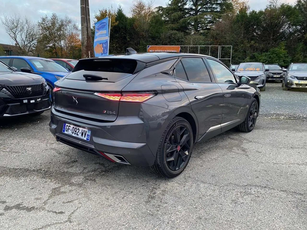 Vue 3/4 arrière droite d'une DS4 gris platinium 2022 avec feux arrière allumés et jantes noires au parking.