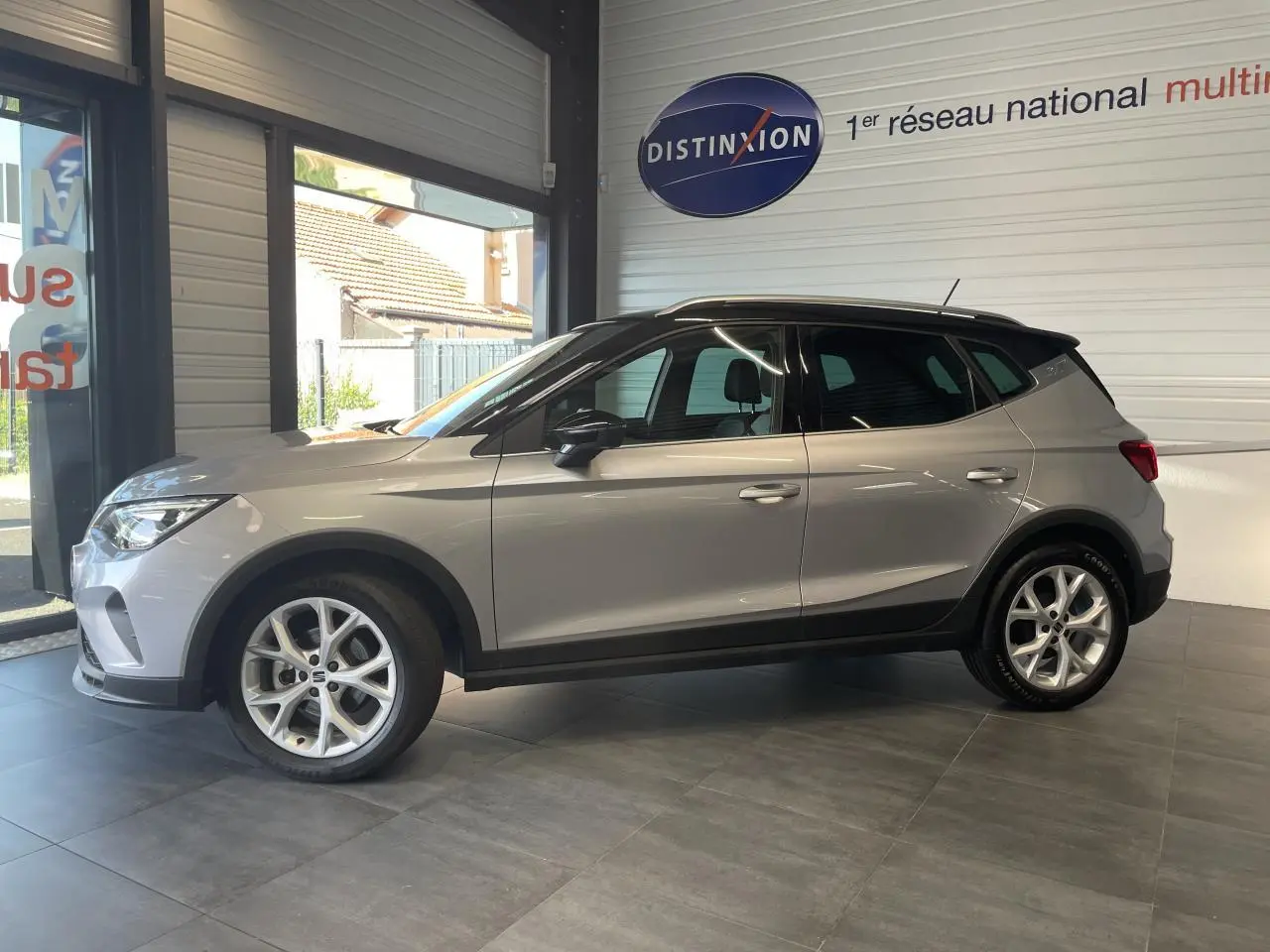 Vue de profil côté gauche d'un SEAT Arona 2024 gris GRS en showroom avec jantes alliage 16 pouces.