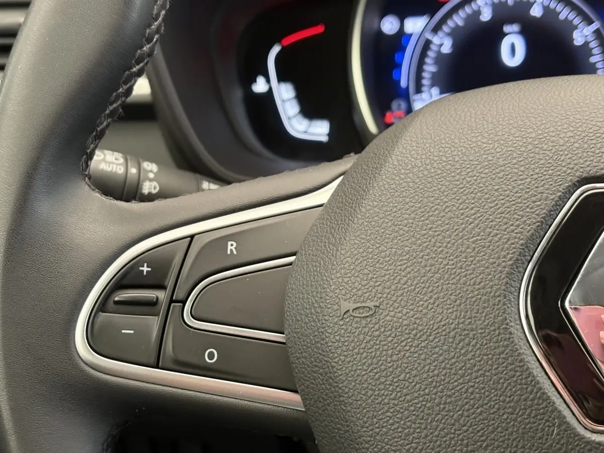 Gros plan sur le volant cuir gris foncé de la Renault Kadjar avec commandes intégrées et tableau de bord lumineux en arrière-plan.