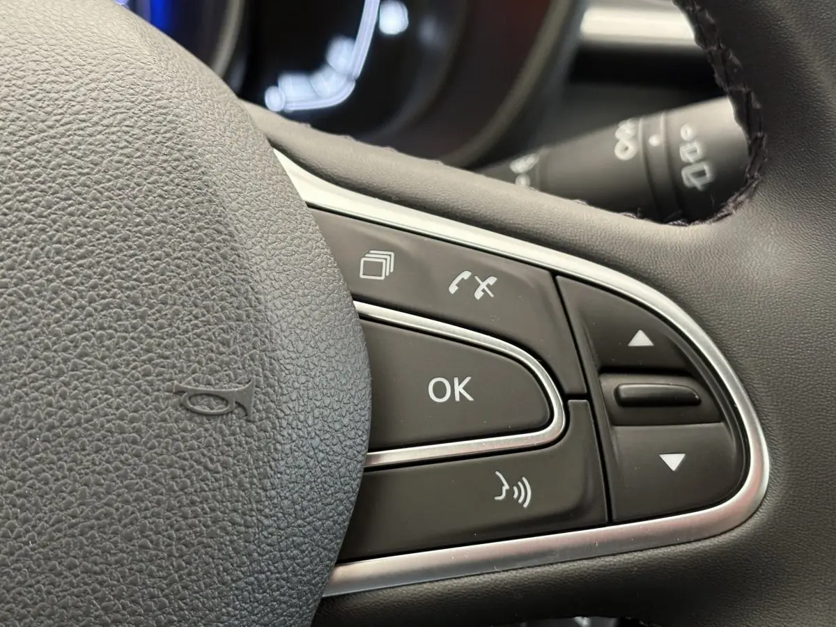 Gros plan sur les commandes au volant cuir noir du Renault Kadjar gris foncé, mettant en valeur les boutons multifonctions.