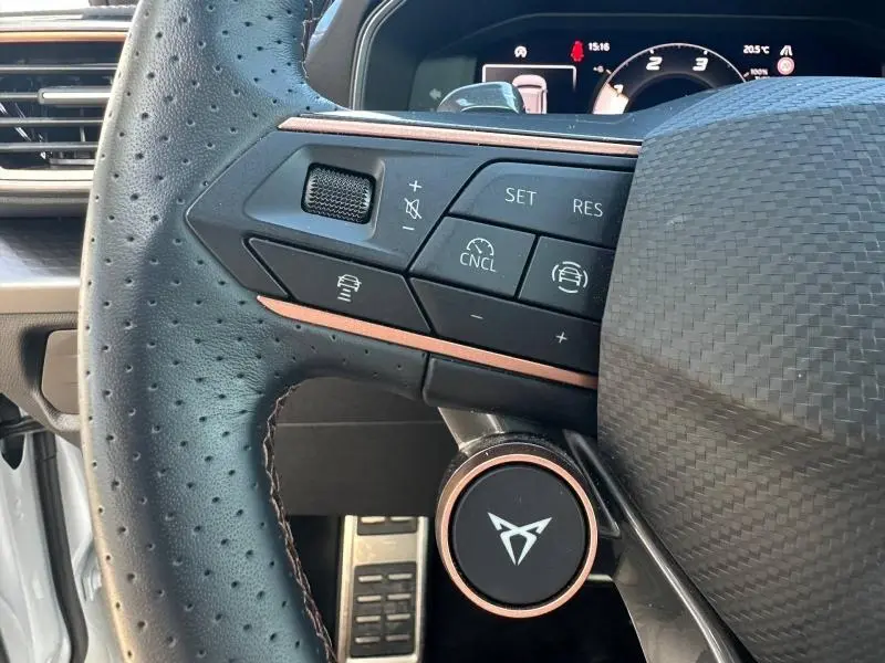 Gros plan sur le volant perforé du CUPRA Formentor blanc Nevada 2025, avec commandes multifonctions et logo central cuivré.