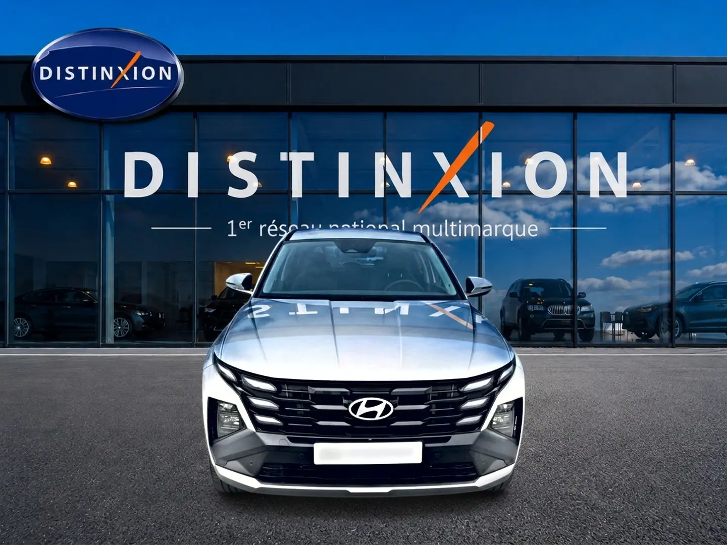 Vue frontale d'un Hyundai Tucson blanc 2026 garé devant une vitrine avec logo Distinxion en reflet.