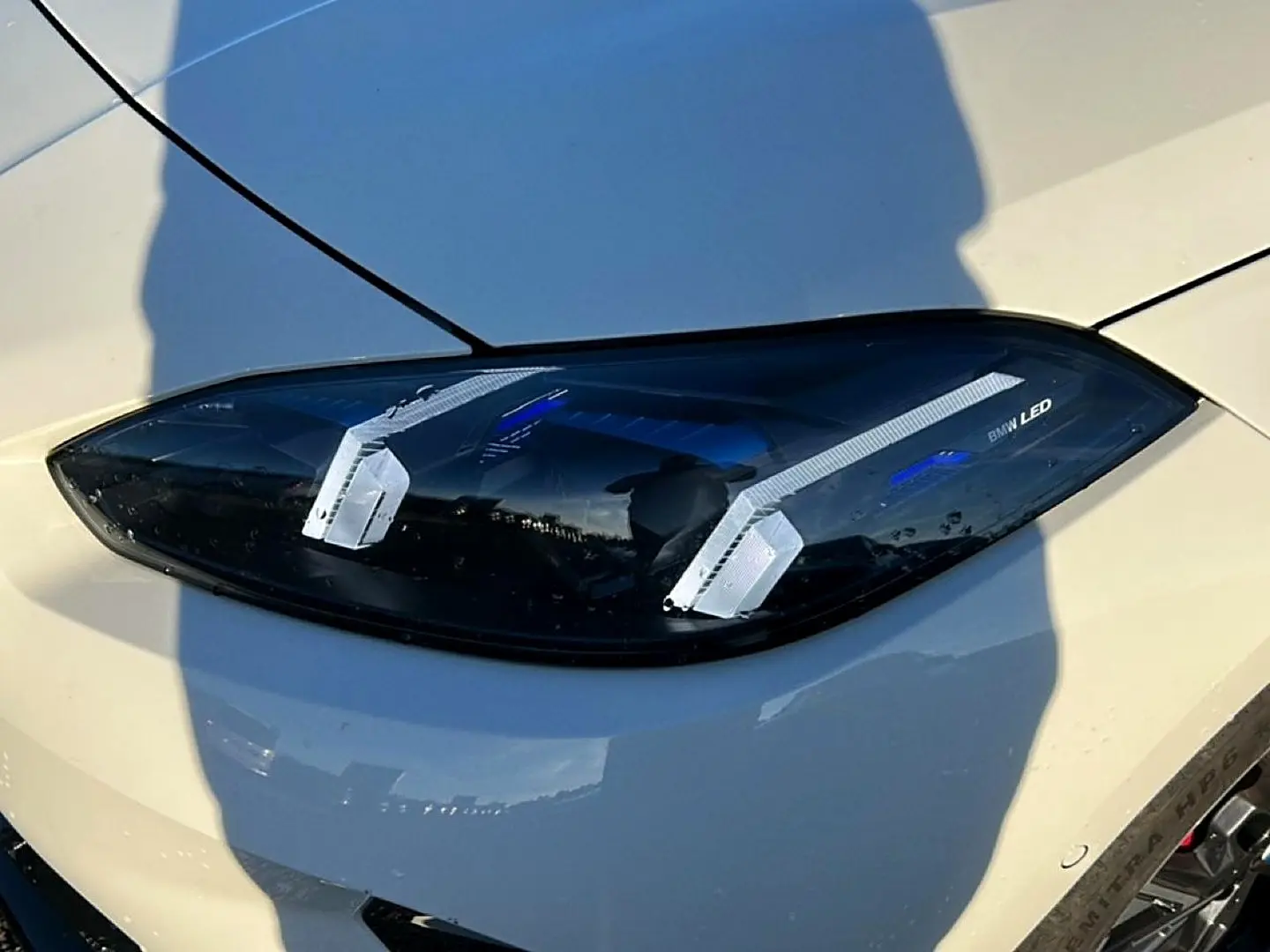 Gros plan sur le phare avant droit LED d'une BMW Série 1 blanche alpin, avec détails lumineux bleus et contours noirs.