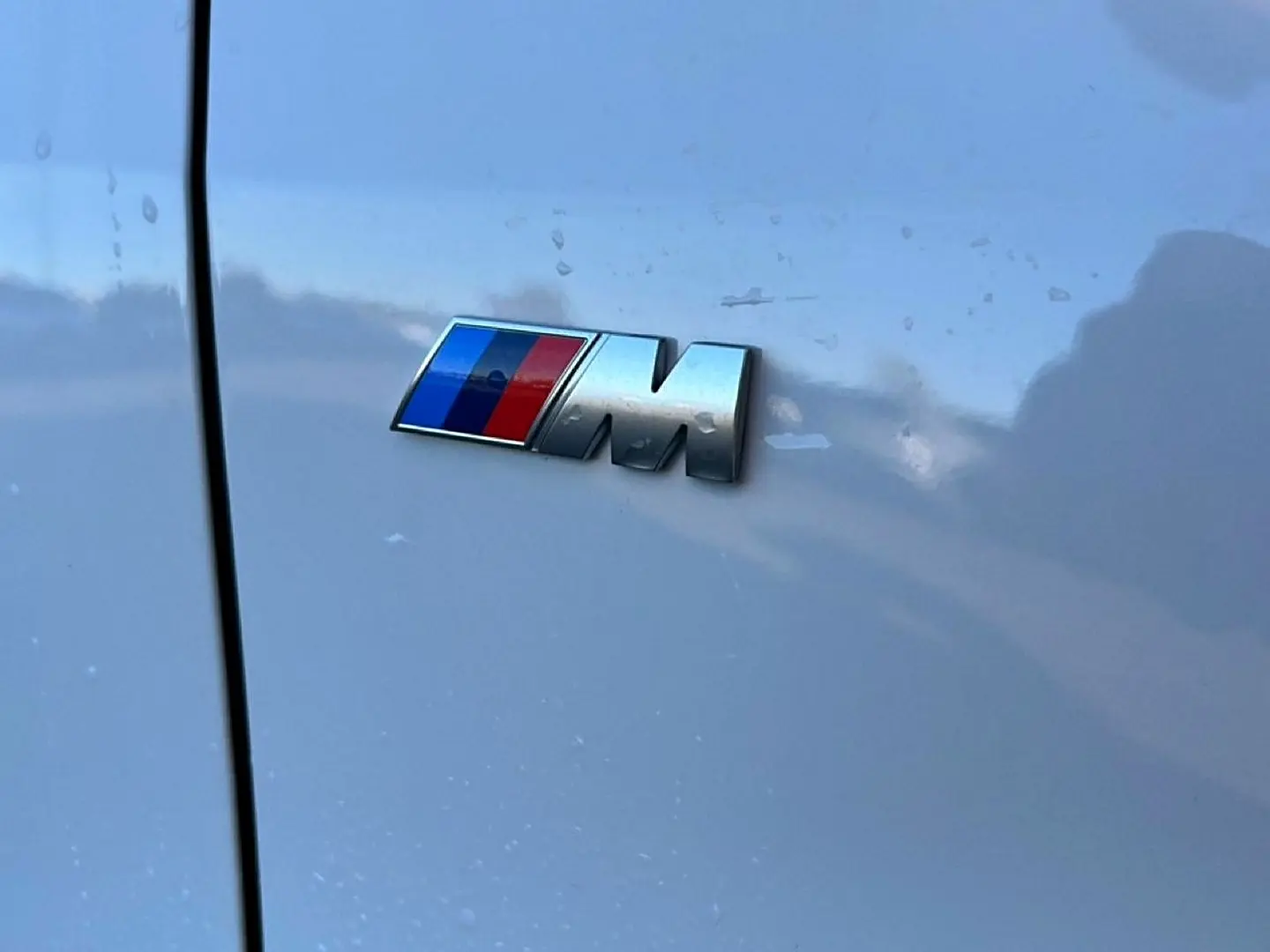 Gros plan sur l'emblème M chromé sur la porte blanche alpin d'une BMW Série 1 2025.