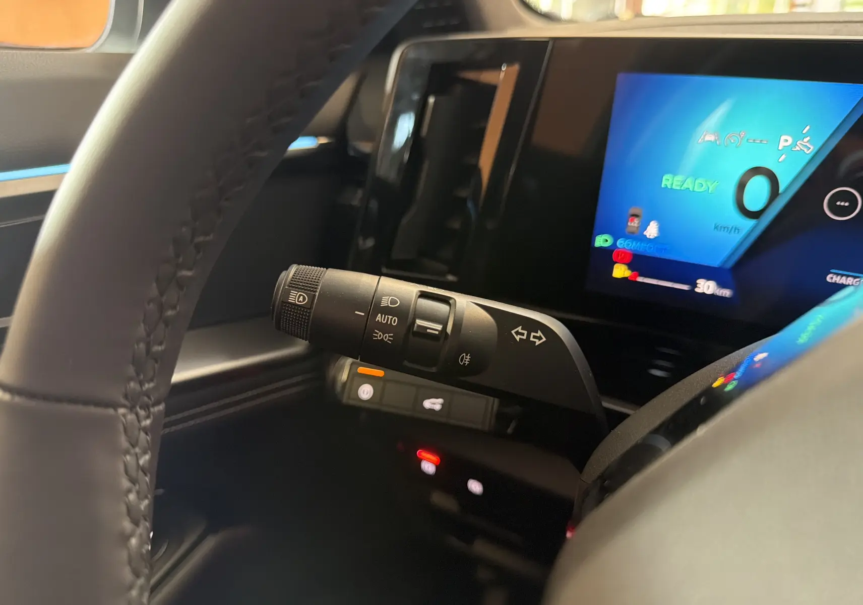 Gros plan intérieur sur la commande des phares et le tableau de bord numérique bleu du Renault Austral E-Tech blanc toit noir.