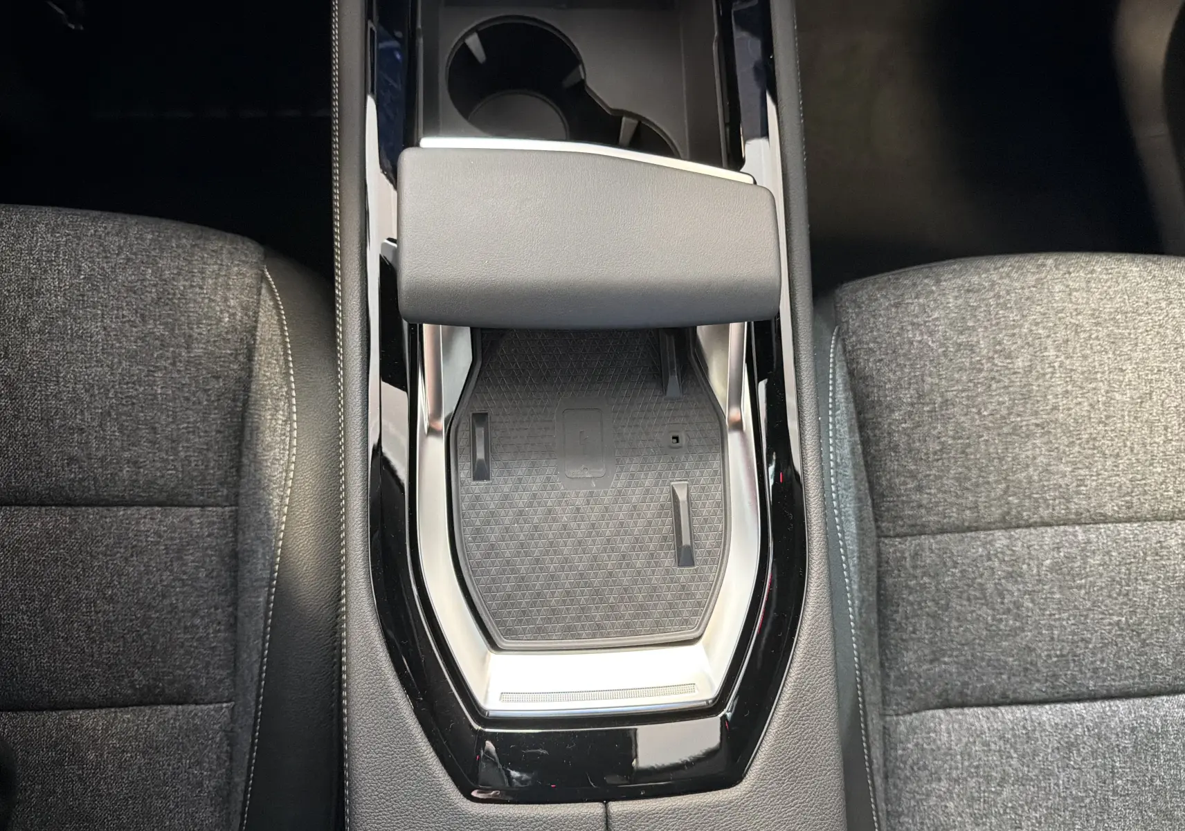 Vue plongeante sur la console centrale noire et gris foncé du Renault Austral E-Tech avec accoudoir et porte-gobelets.