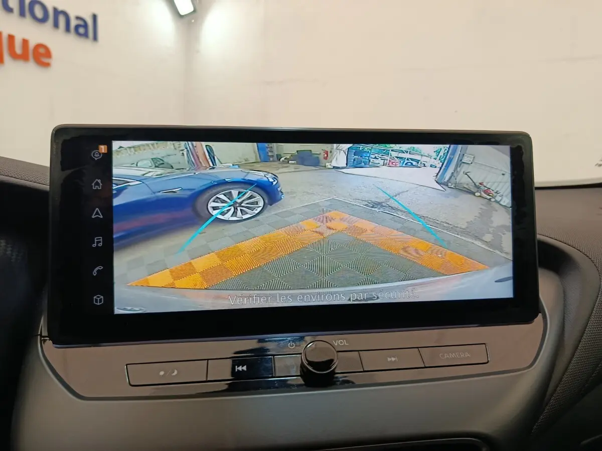 Écran tactile du Nissan Juke 2025 montrant la caméra de recul avec vue sur une voiture bleue à gauche.