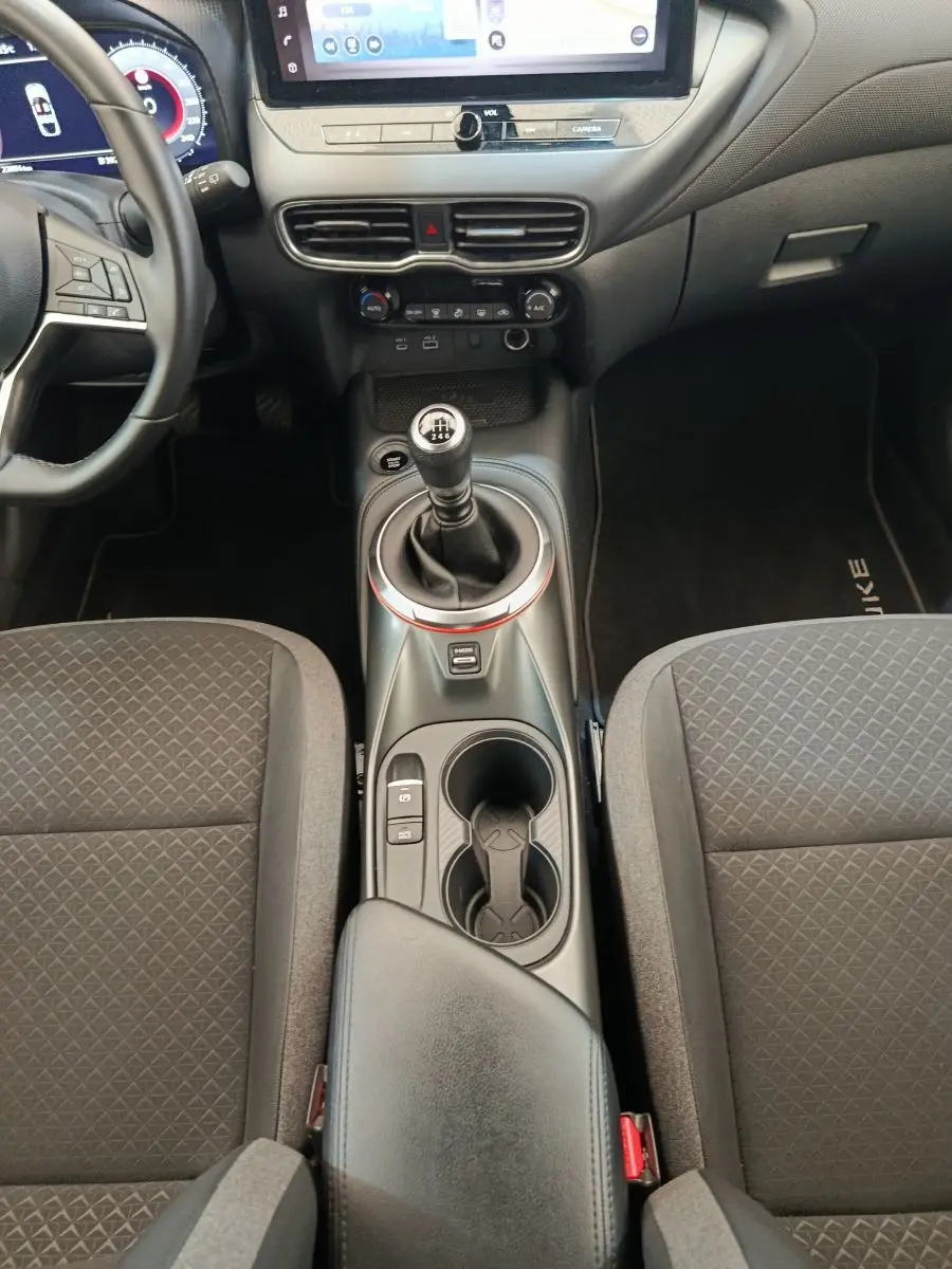 Vue intérieure centrée sur la console centrale et levier de vitesse manuel, sièges tissu gris et volant multifonctions Nissan Juke.