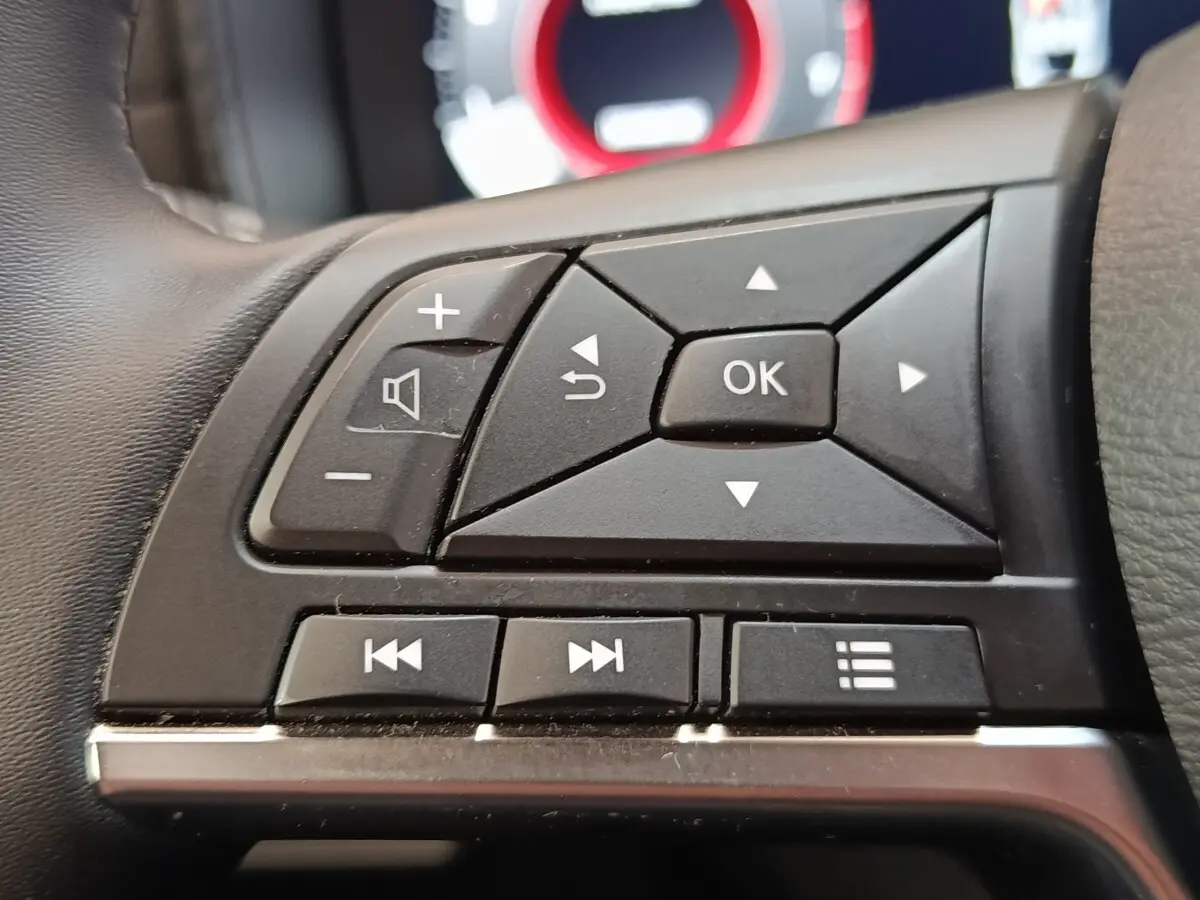Gros plan sur les commandes multifonctions noires du volant du Nissan Juke 2025, version essence gris clair.