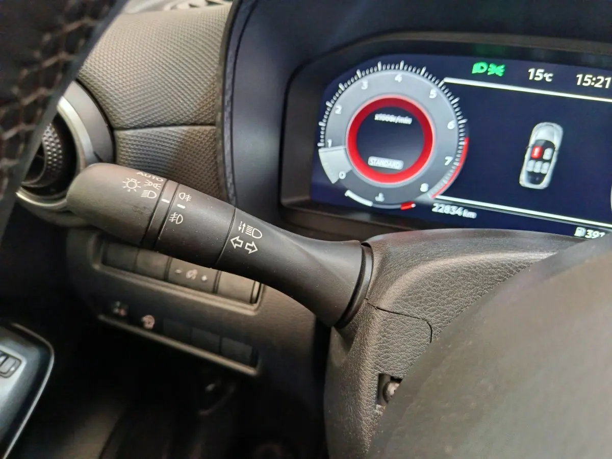 Gros plan sur la manette de clignotants noire à gauche du volant, avec tableau de bord numérique affichant 22 834 km.
