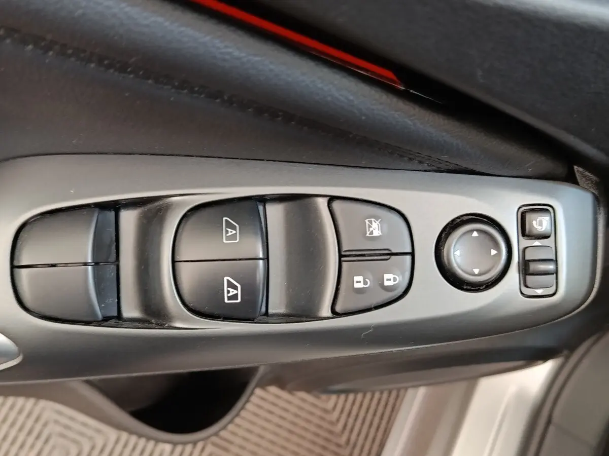 Gros plan sur les commandes de lève-vitres, verrouillage et réglage des rétroviseurs côté conducteur d'un Nissan Juke gris clair.