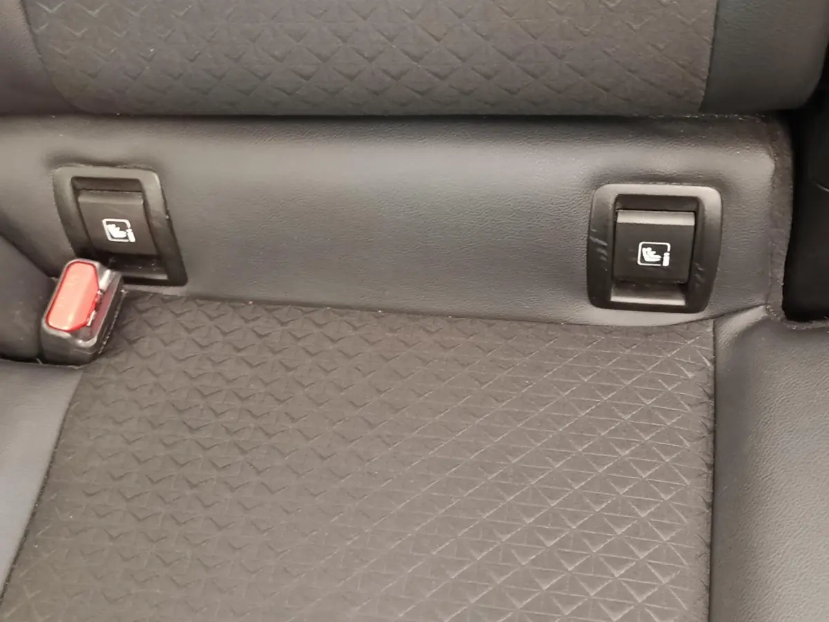 Gros plan sur la banquette arrière gris foncé du Nissan Juke 2025 avec fixation Isofix et boucle de ceinture rouge visible.