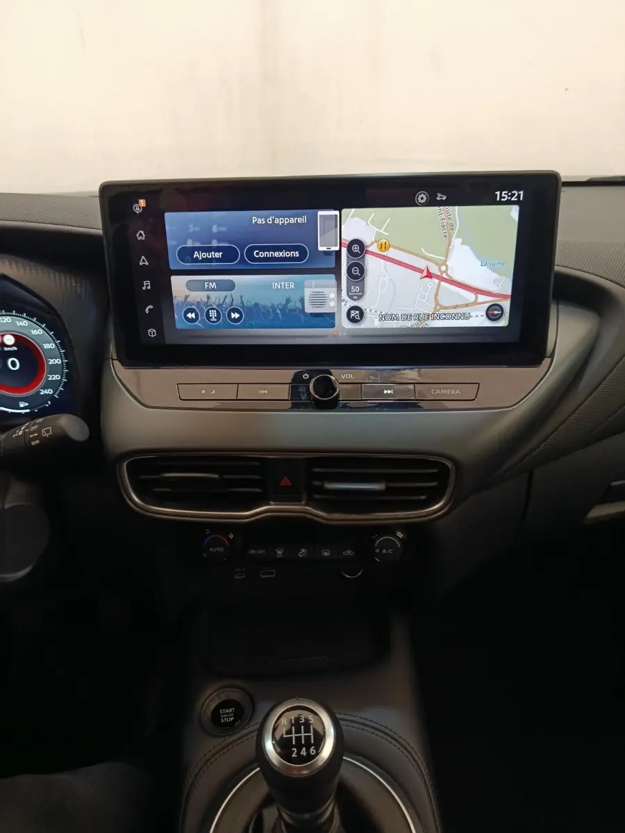Vue intérieure centrée sur la console centrale du Nissan Juke gris clair 2025 avec écran tactile et levier de vitesses manuel.