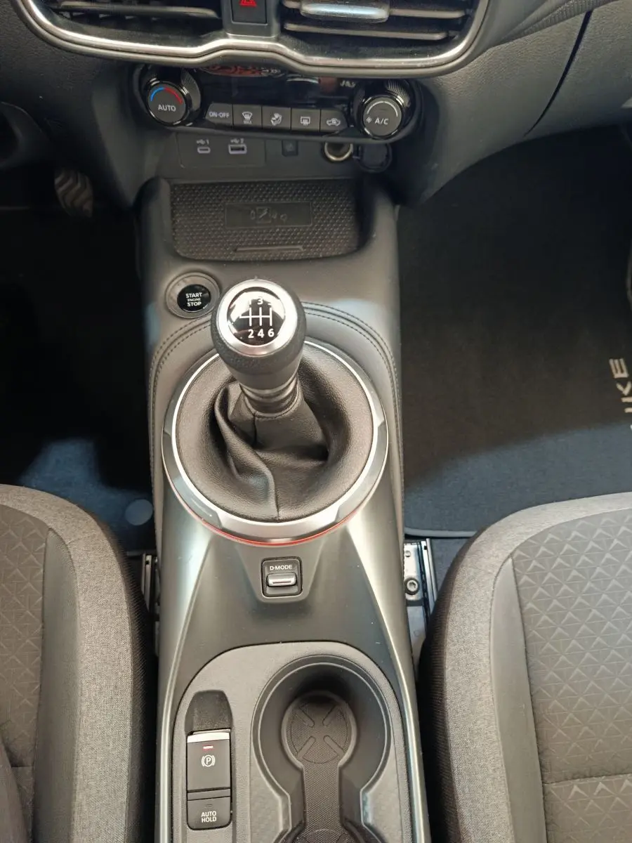 Vue rapprochée de la console centrale du Nissan Juke gris clair 2025 avec levier de vitesse manuel et commandes climatisation.