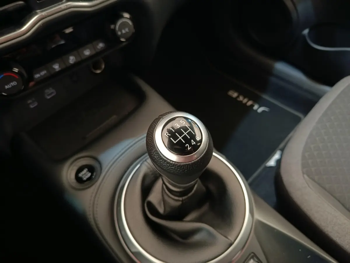Gros plan sur le levier de vitesses manuel du Nissan Juke gris clair, avec console centrale et tapis marqué Juke visible.