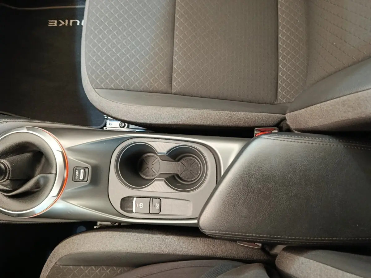 Vue plongeante sur la console centrale noire avec boîte manuelle et accoudoir entre les sièges gris du Nissan Juke 2025.