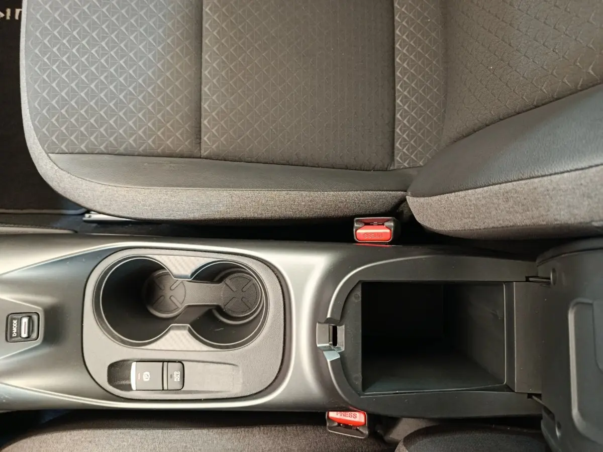 Vue plongeante sur la console centrale noire du Nissan Juke gris clair, avec porte-gobelets et accoudoir ouvert.