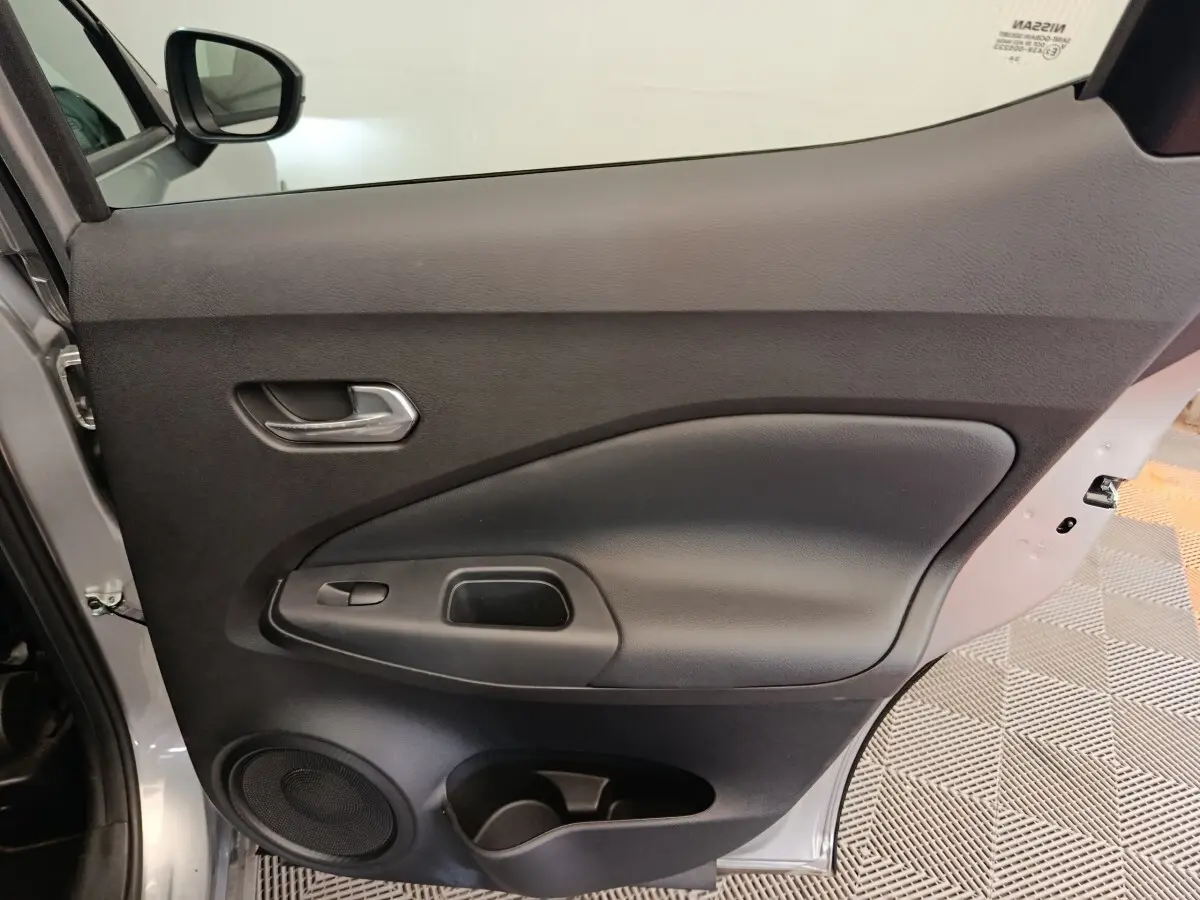 Vue intérieure côté gauche de la porte avant gris clair du Nissan Juke 2025 avec poignée et haut-parleur intégrés.