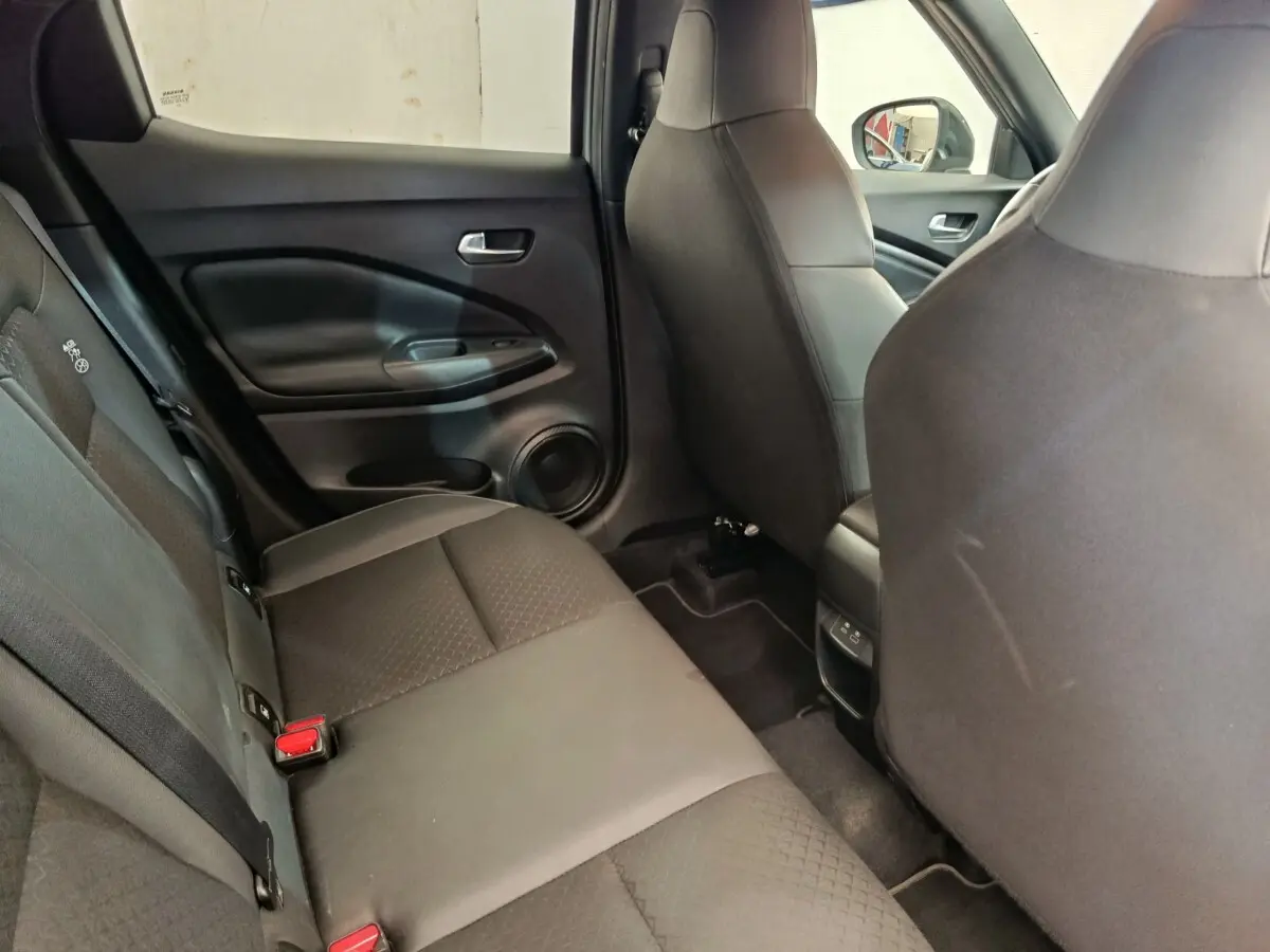 Vue intérieure arrière côté gauche du Nissan Juke 2025, sièges tissu gris foncé avec ceintures visibles.