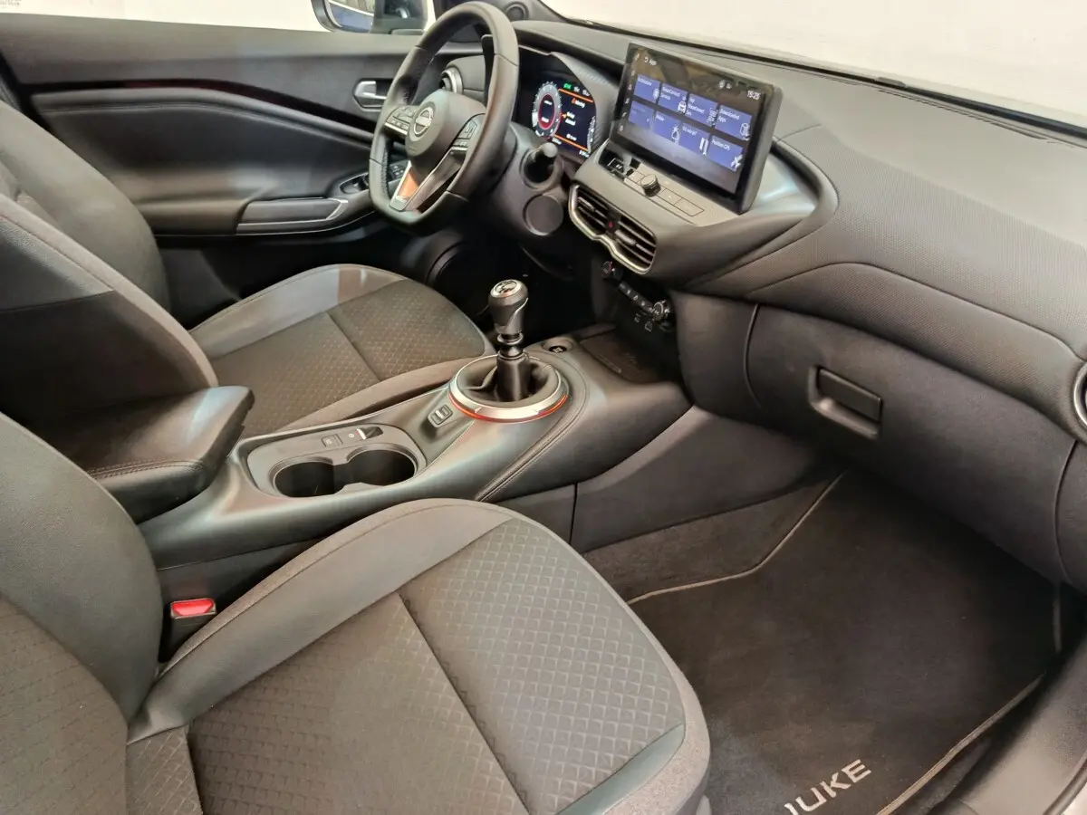 Vue intérieure côté passager du Nissan Juke 2025, montrant la console centrale avec levier de vitesse manuel et écran tactile.