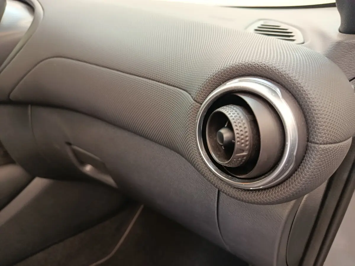 Détail de la sortie d'air ronde chromée côté passager du tableau de bord gris foncé du Nissan Juke 2025.