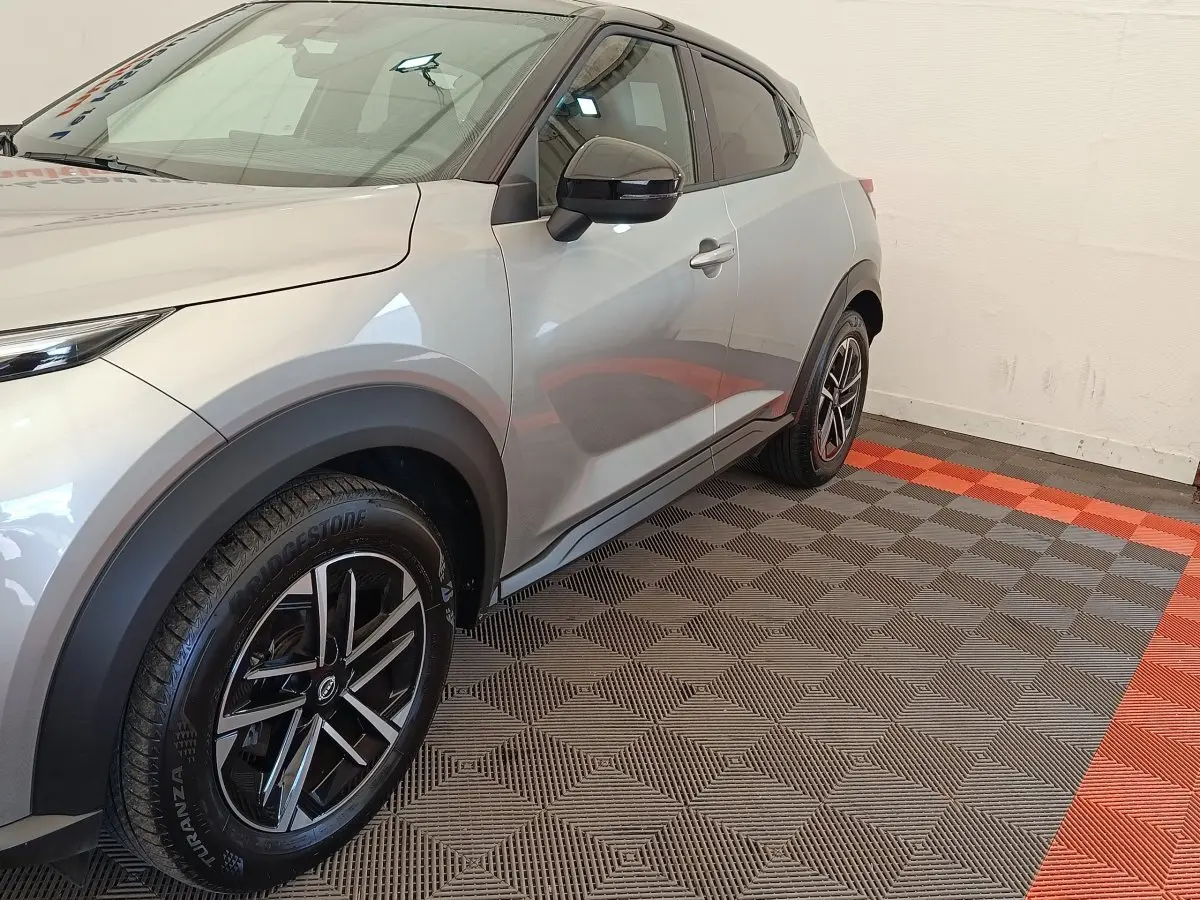 Vue 3/4 avant droit du Nissan Juke gris clair, soulignant ses jantes noires et détails de carrosserie lisse.