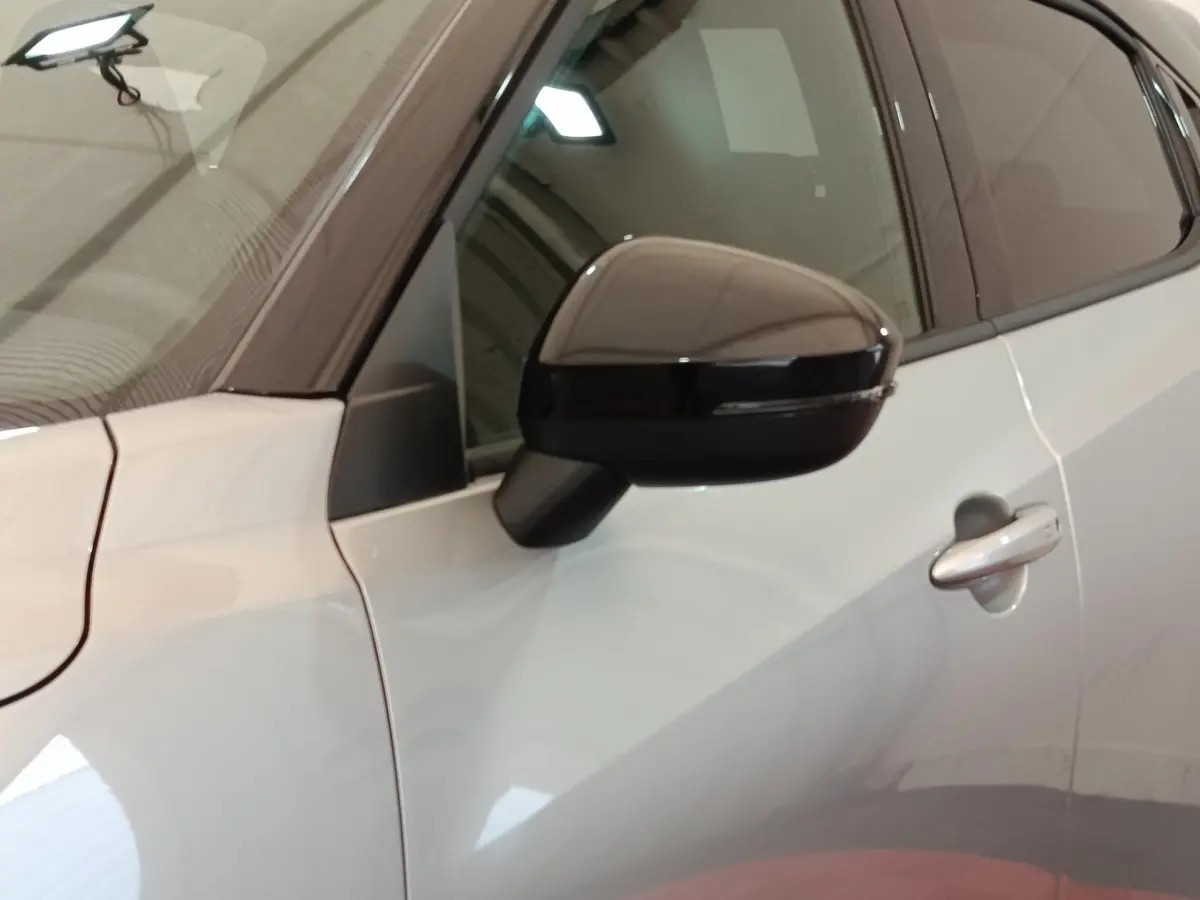 Vue rapprochée du côté gauche d’un Nissan Juke gris clair, mettant en valeur le rétroviseur noir et la poignée de porte.