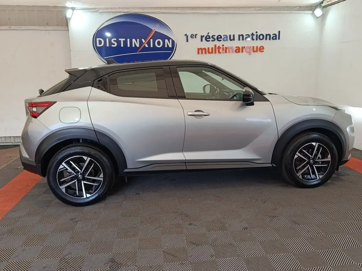 Nissan Juke gris clair vue de profil côté gauche, avec toit noir et jantes alliage noires en intérieur showroom.
