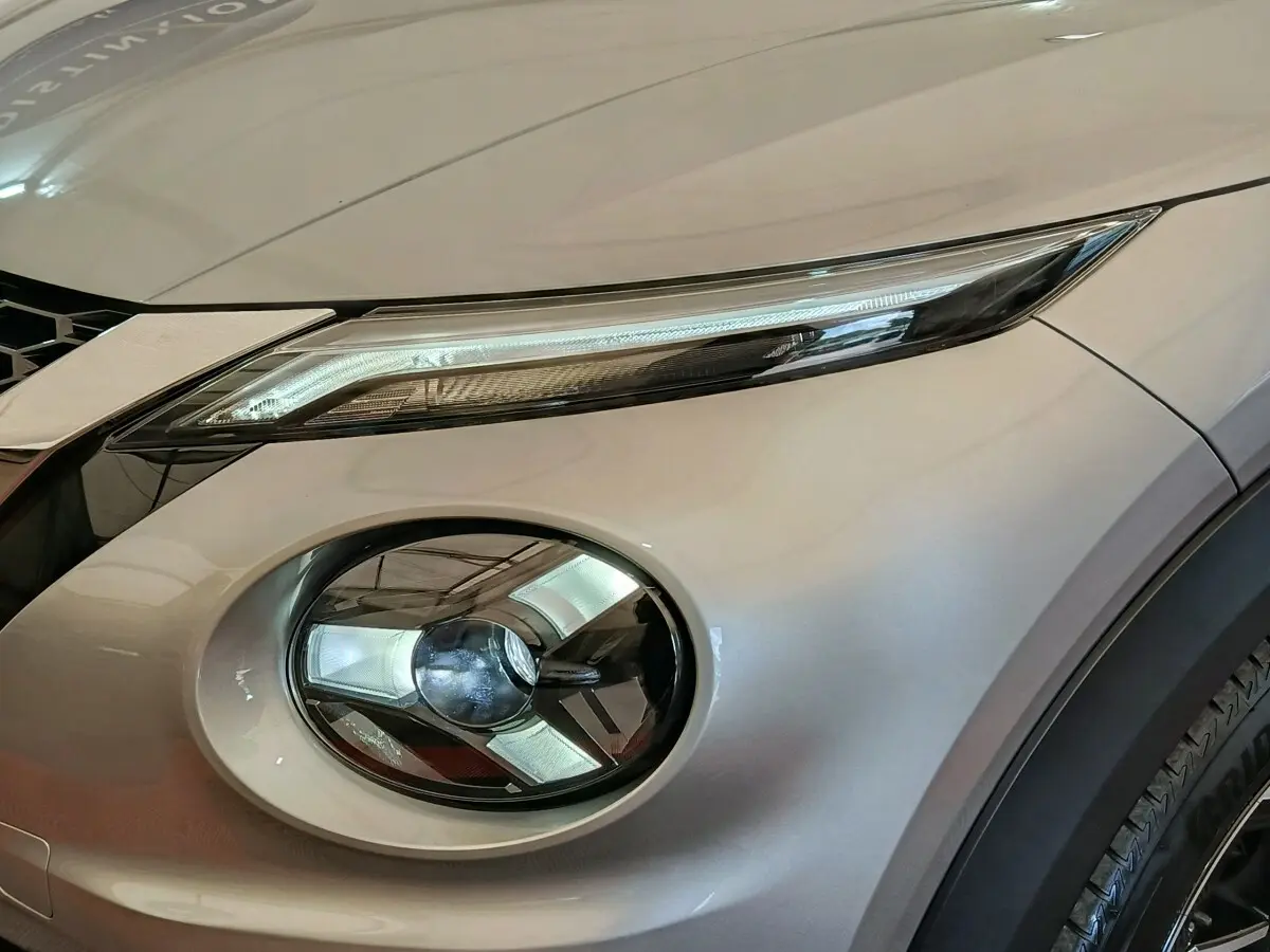 Gros plan sur le phare avant droit gris clair du Nissan Juke 2025 avec éclairage LED et partie de la calandre visible.