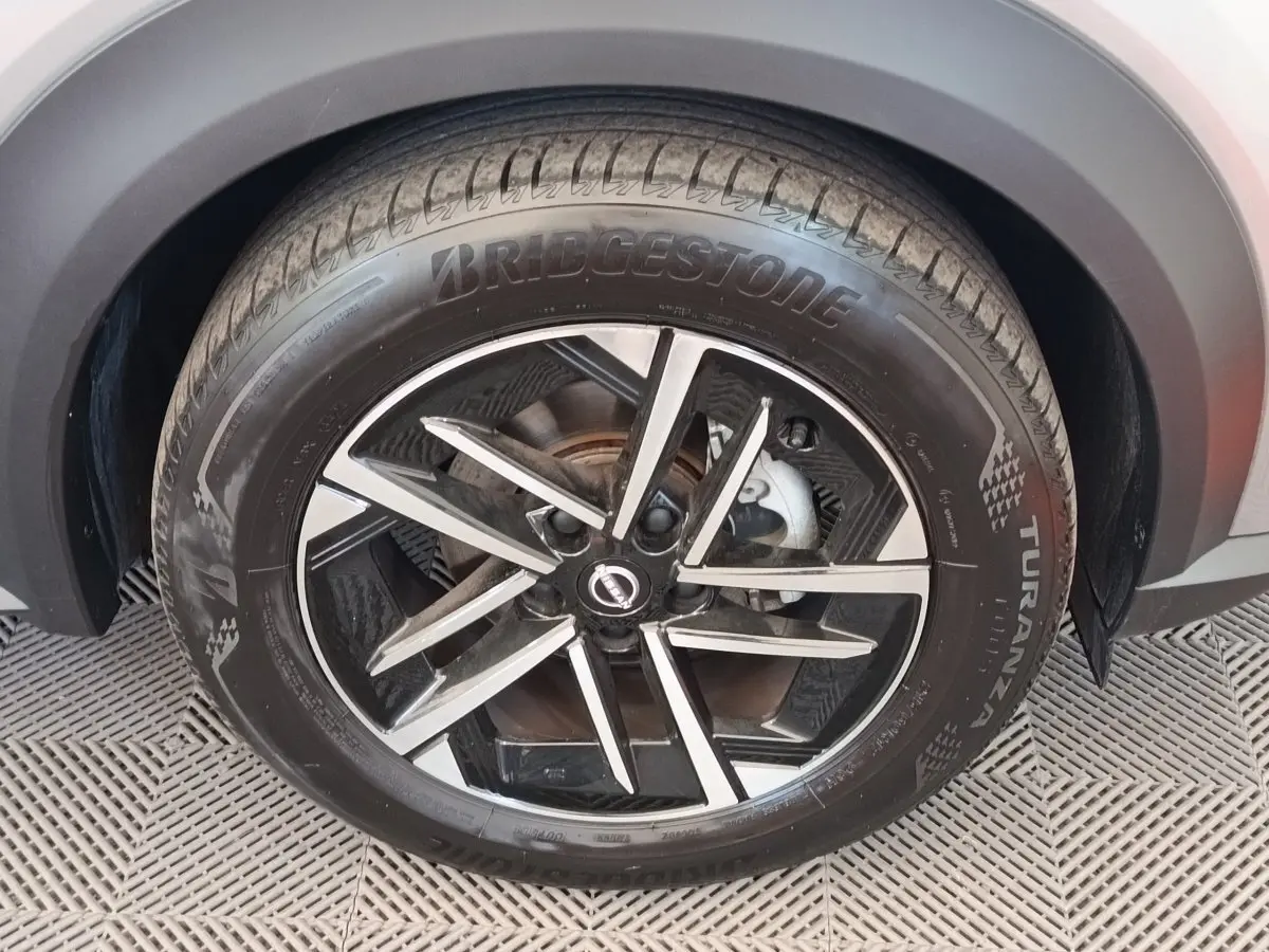 Gros plan sur la roue avant droite du Nissan Juke gris clair, avec jante alliage noire et argentée.