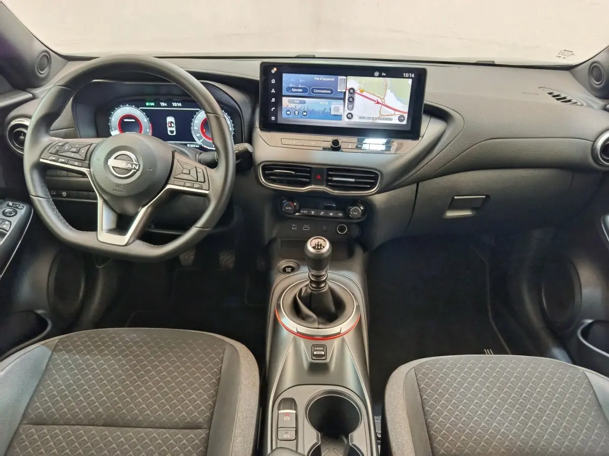 Vue intérieure avant du Nissan Juke DIG-T 114 BVM6 Acenta 2025, tableau de bord noir avec écran tactile et levier de vitesse manuel.
