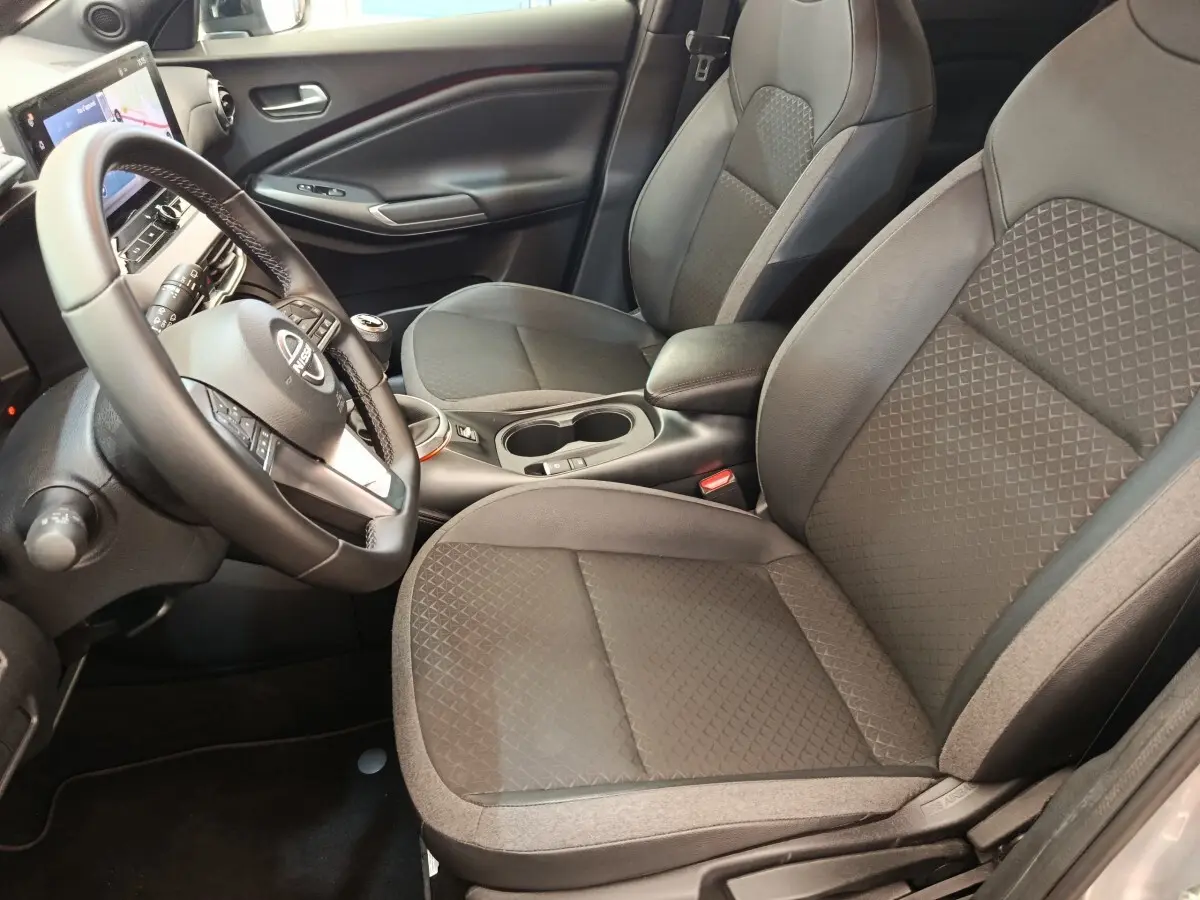 Vue intérieure avant droite du Nissan Juke 2025 gris clair, avec volant multifonctions et sièges tissu gris à motifs géométriques.