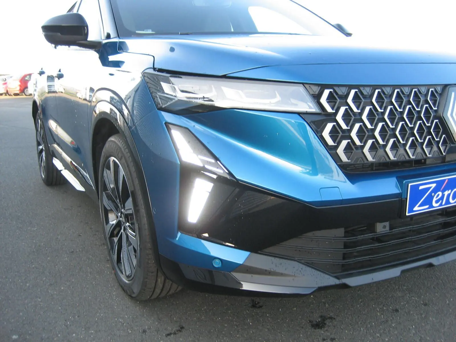 Vue 3/4 avant gauche du Renault Austral bleu outremer avec toit noir, mettant en valeur sa calandre hexagonale et ses feux LED distinctifs.