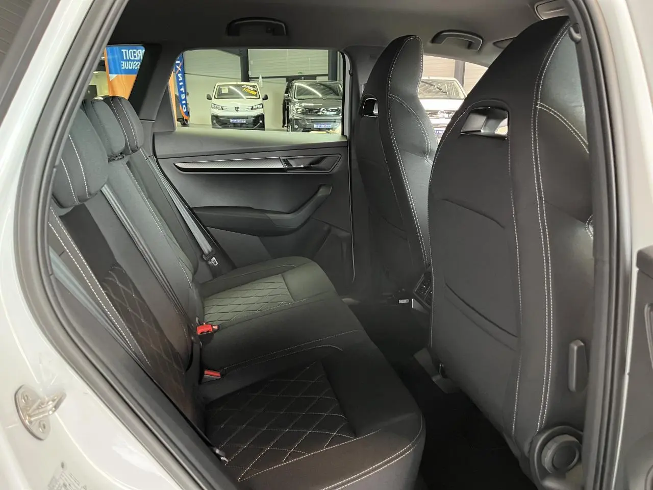Vue intérieure côté gauche des sièges arrière noirs en tissu avec surpiqûres blanches du Skoda Karoq blanc 2025 Sportline.