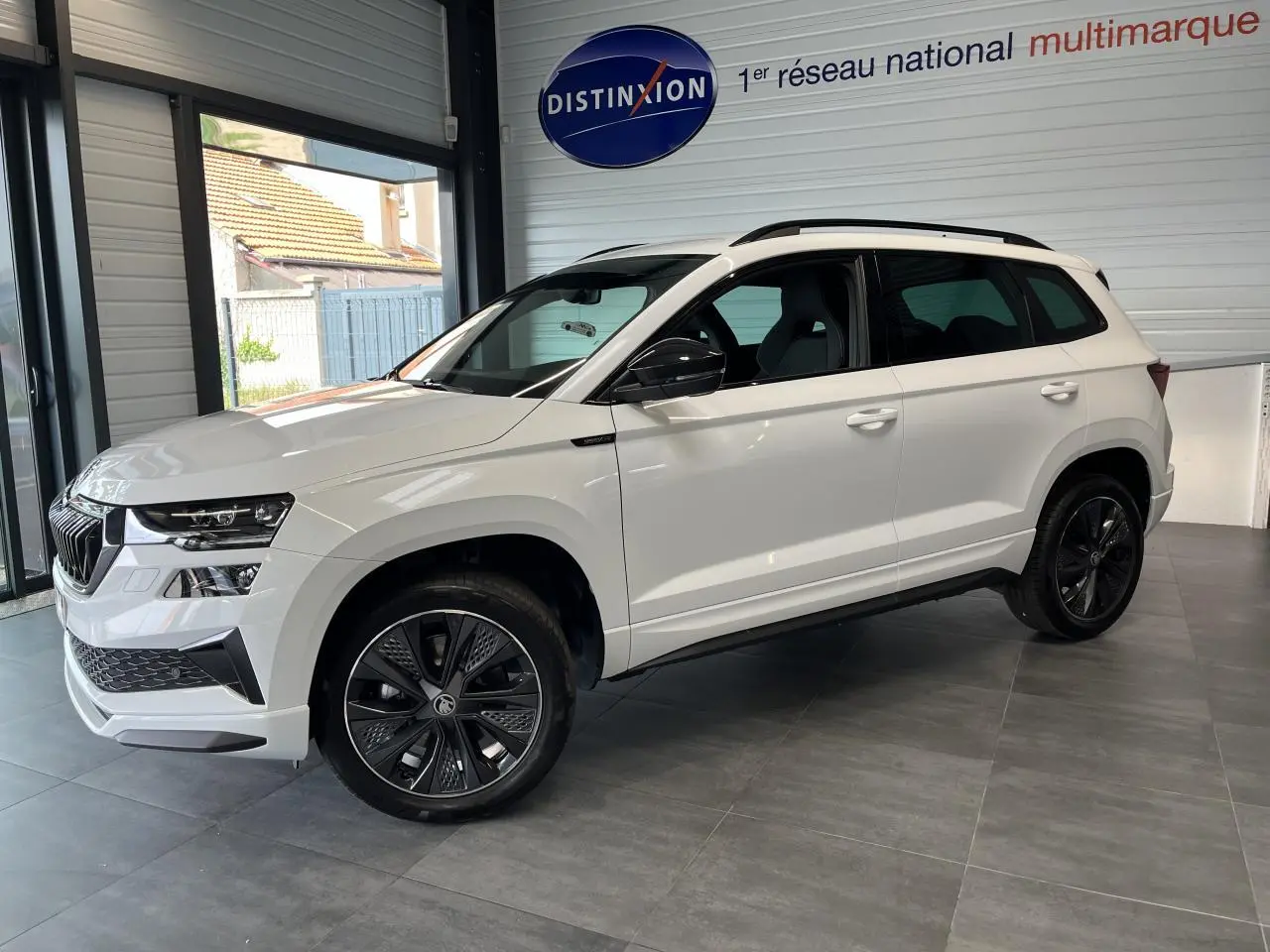 Vue 3/4 avant droite d'un SUV Skoda Karoq blanc avec jantes noires et rétroviseurs noirs dans un showroom.
