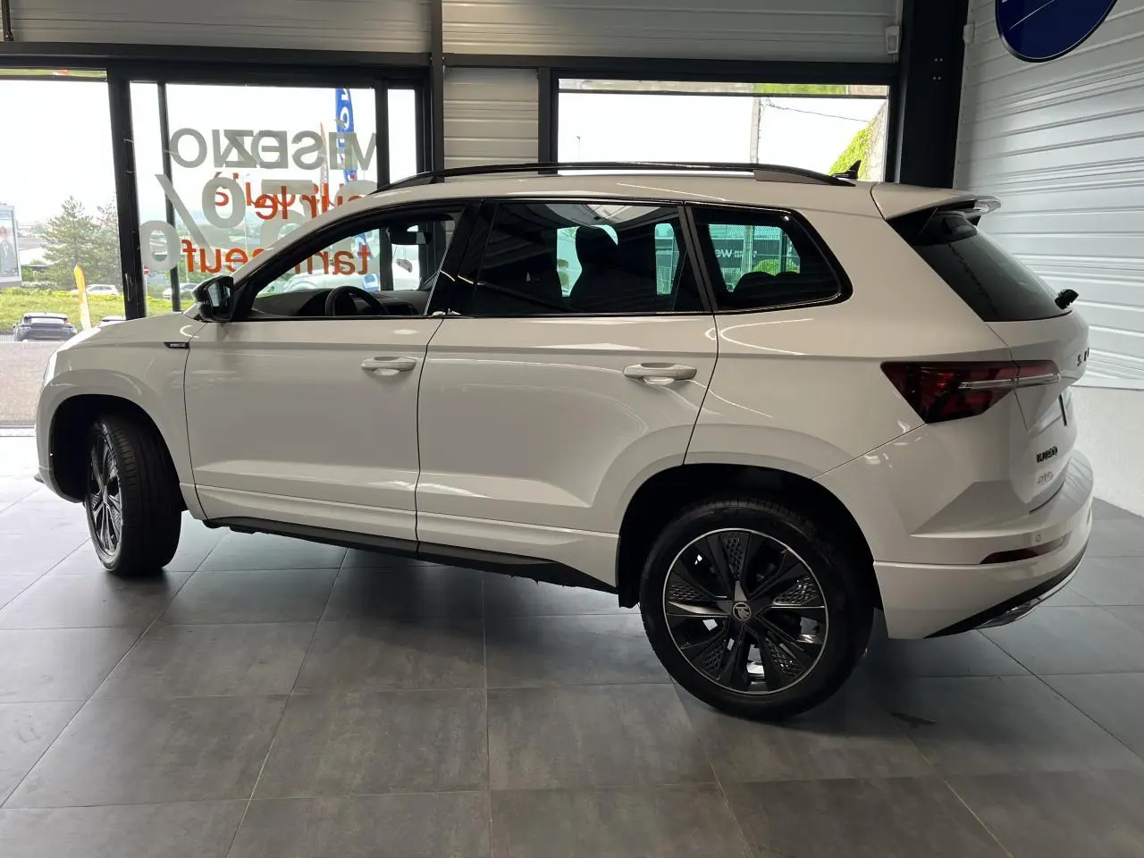 Profil droit du SUV blanc SKODA KAROQ 2025 Sportline avec jantes alliage noires et toit noir brillant.