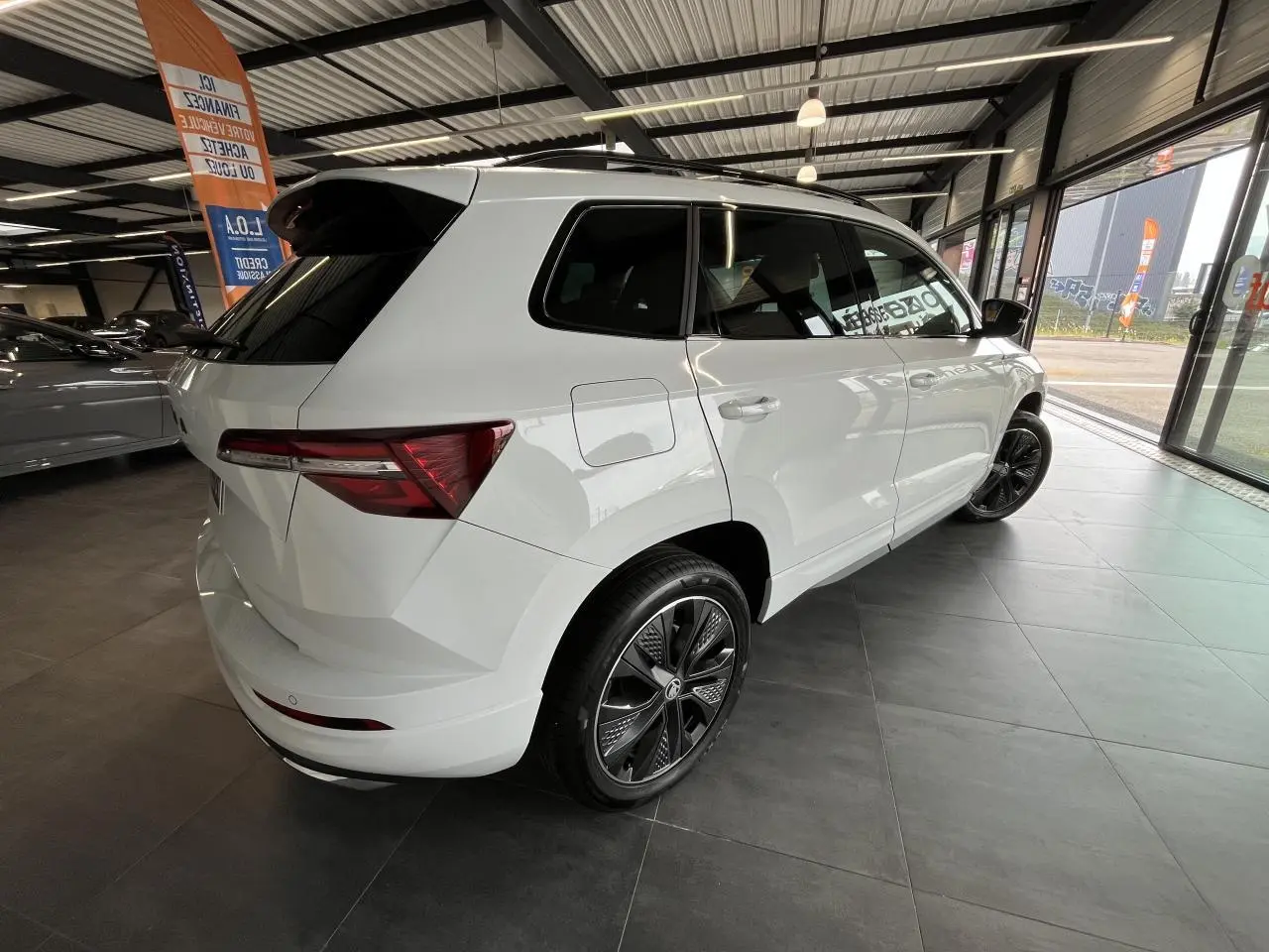 Vue 3/4 arrière droite d'un SUV SKODA KAROQ blanc avec jantes alliage noires et toit noir en showroom.
