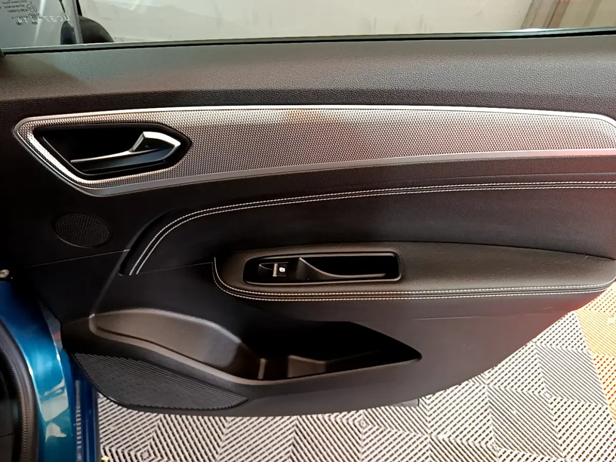 Vue intérieure du panneau de porte avant gauche bleu du Renault Arkana 2023 avec surpiqûres blanches et insert décoratif argenté.