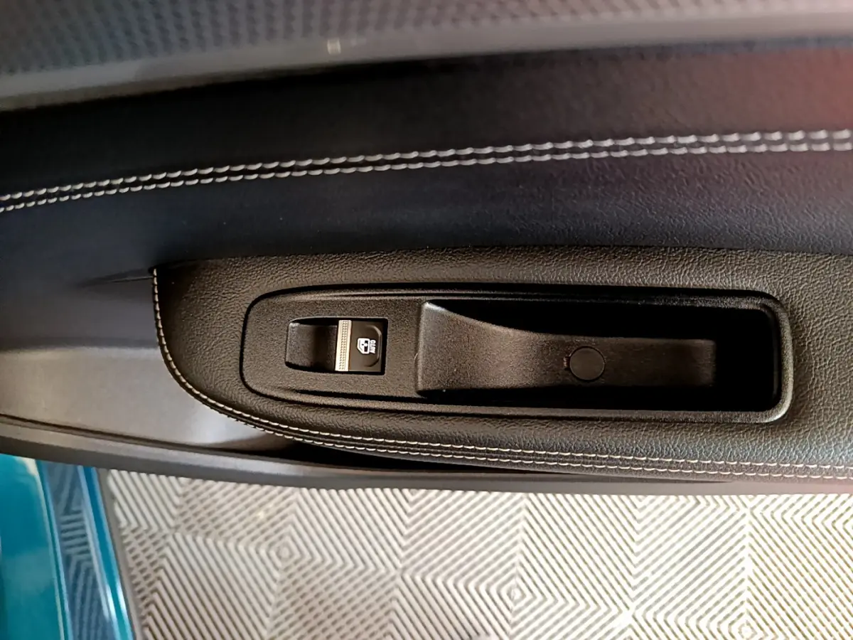 Détail de la poignée intérieure noire avec bouton de verrouillage sur la porte côté gauche d’une Renault Arkana bleu.