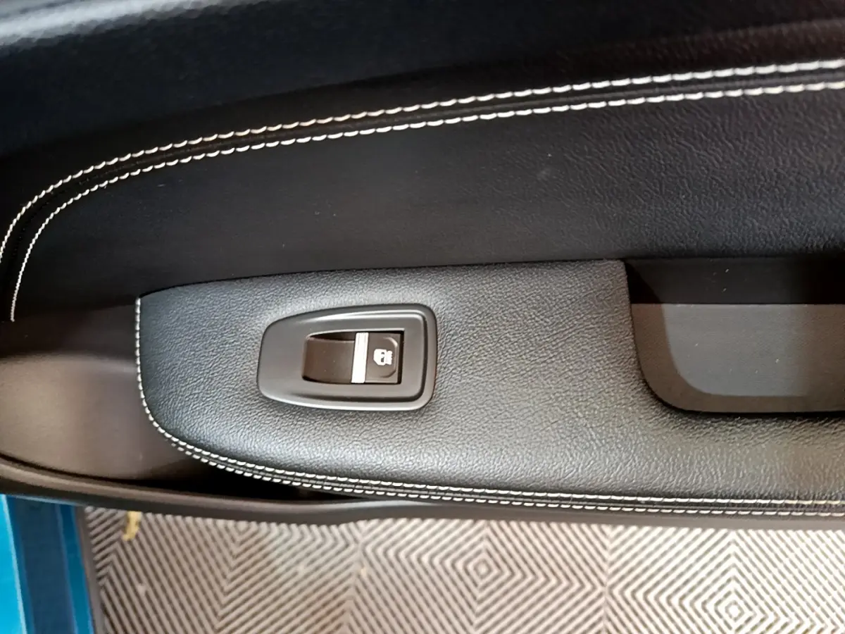 Détail de la commande de verrouillage centralisé sur la portière intérieure noire avec surpiqûres blanches du Renault Arkana bleu.