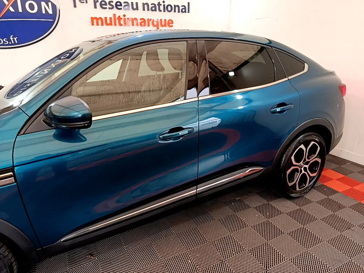 Profil droit du Renault Arkana Techno E-Tech hybride bleu 2023, mettant en valeur ses jantes distinctives et lignes fluides.