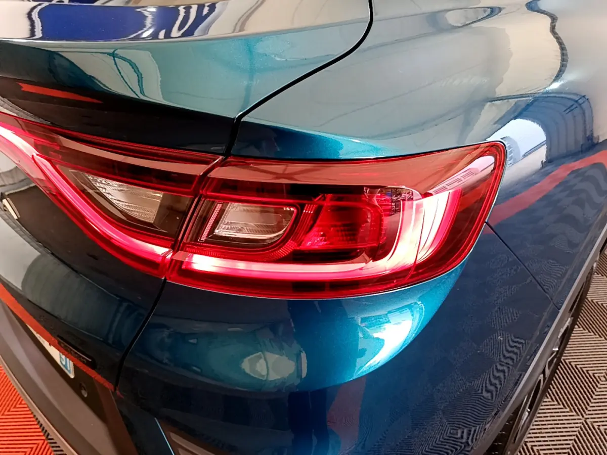 Gros plan sur le feu arrière droit rouge d’un Renault Arkana bleu métallisé, avec reflet sur la carrosserie lisse.