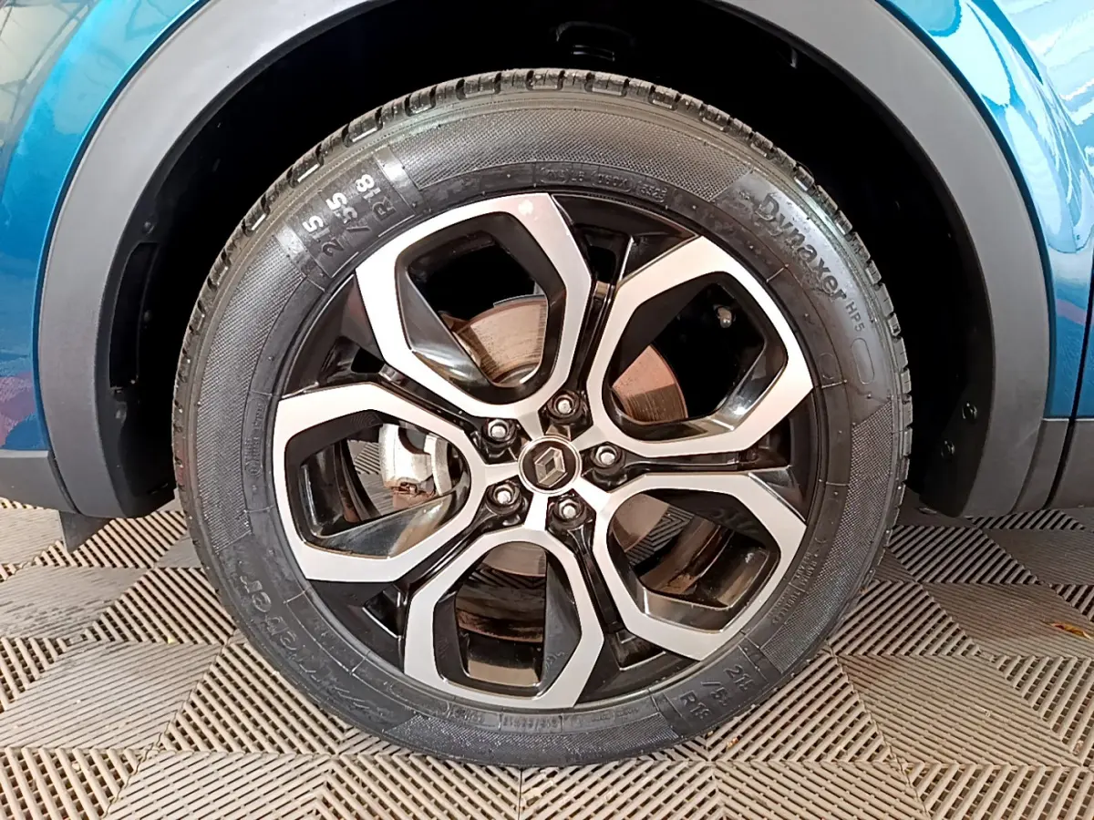 Gros plan sur la roue avant droite du Renault Arkana bleu, mettant en valeur la jante alliage noire et argentée au design moderne.