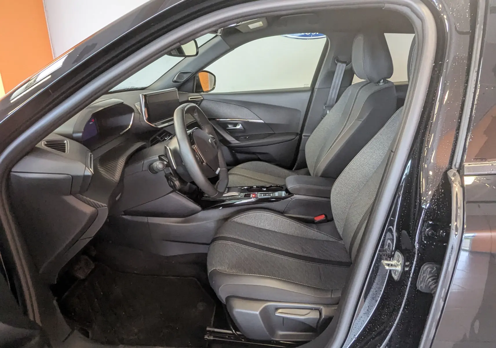 Vue intérieure côté conducteur du Peugeot 2008 noir 2024, mettant en valeur les sièges tissu et la console centrale moderne.