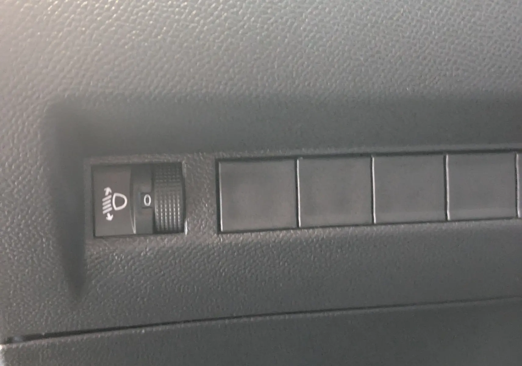 Gros plan sur le réglage de hauteur des phares dans l'habitacle noir du Peugeot 2008 130ch eat8 allure 2024.
