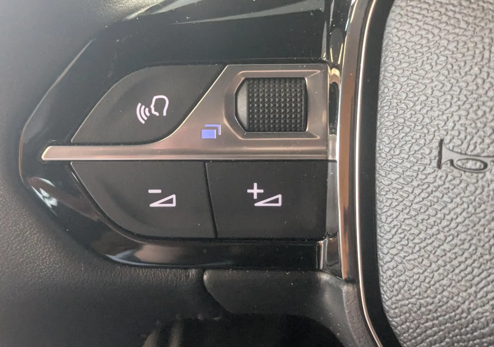 Gros plan sur les commandes de volume et de reconnaissance vocale sur le volant noir du Peugeot 2008 130ch eat8 allure 2024.