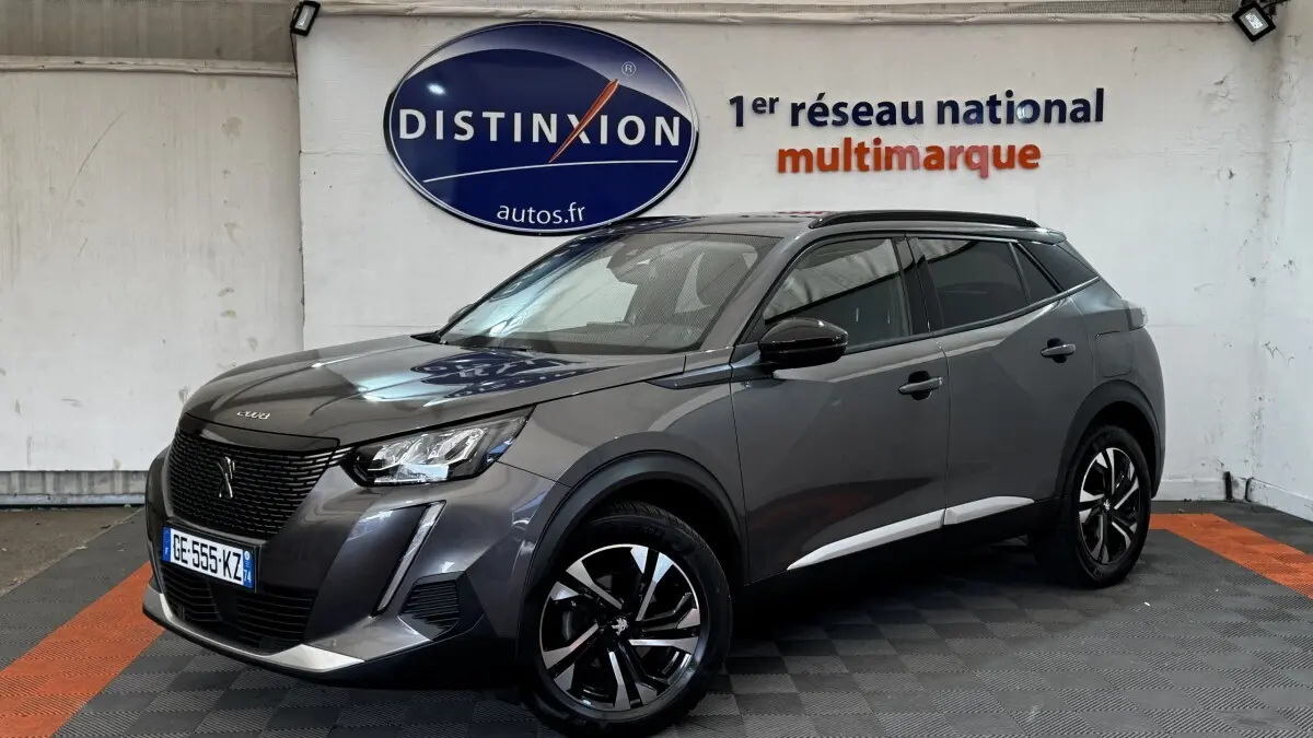 Peugeot 2008 gris foncé vue en 3/4 avant droit, avec jantes noires et toit panoramique visible en intérieur showroom.