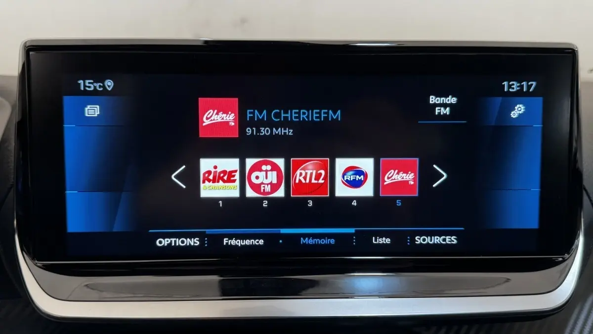 Écran tactile central de la Peugeot 2008 gris foncé affichant les stations radio FM en interface moderne.